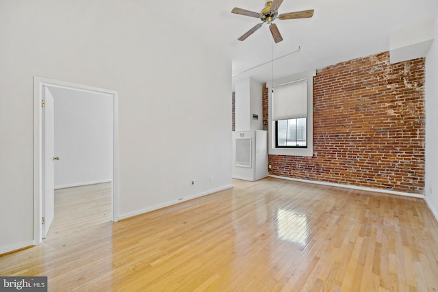 empty room with brick wall, ceiling fan, and light hardwood / wood-style floors