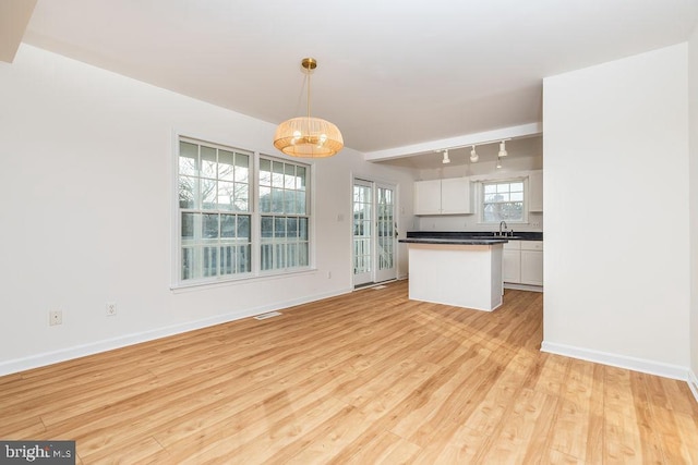 kitchen featuring pendant lighting, sink, rail lighting, light wood-type flooring, and white cabinetry