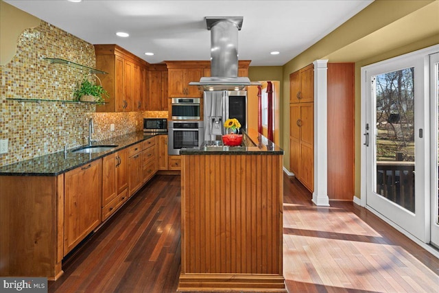 kitchen with backsplash, a kitchen island, appliances with stainless steel finishes, island exhaust hood, and a sink