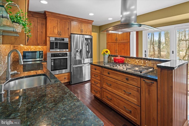 kitchen with brown cabinetry, appliances with stainless steel finishes, island exhaust hood, and a sink