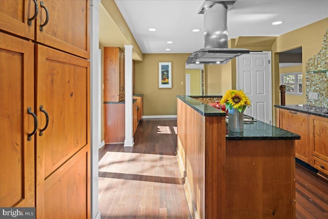 kitchen with a center island, brown cabinetry, dark stone countertops, island range hood, and dark wood-style floors