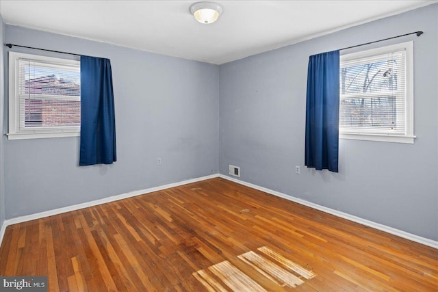 empty room featuring a wealth of natural light, visible vents, and wood finished floors