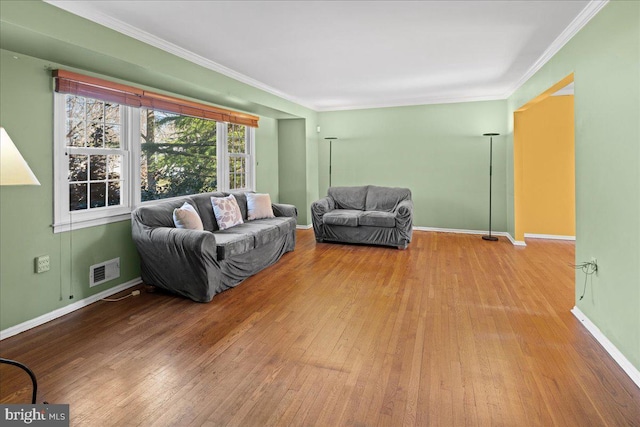 living room featuring hardwood / wood-style floors, baseboards, visible vents, and ornamental molding