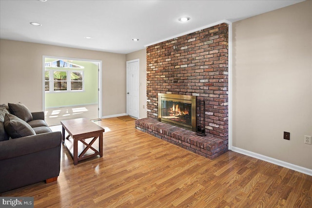 living area with recessed lighting, baseboards, a brick fireplace, and wood finished floors