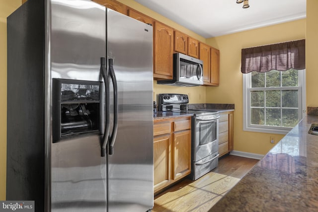 kitchen with appliances with stainless steel finishes, light hardwood / wood-style floors, and dark stone countertops