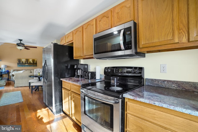 kitchen featuring stone counters, appliances with stainless steel finishes, hardwood / wood-style flooring, and ceiling fan