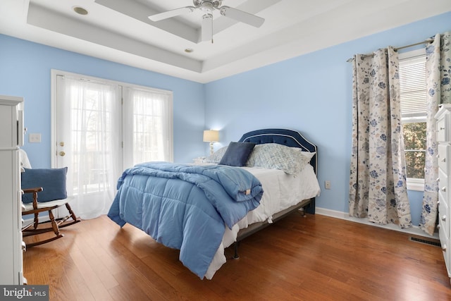 bedroom with dark hardwood / wood-style flooring, a raised ceiling, and ceiling fan