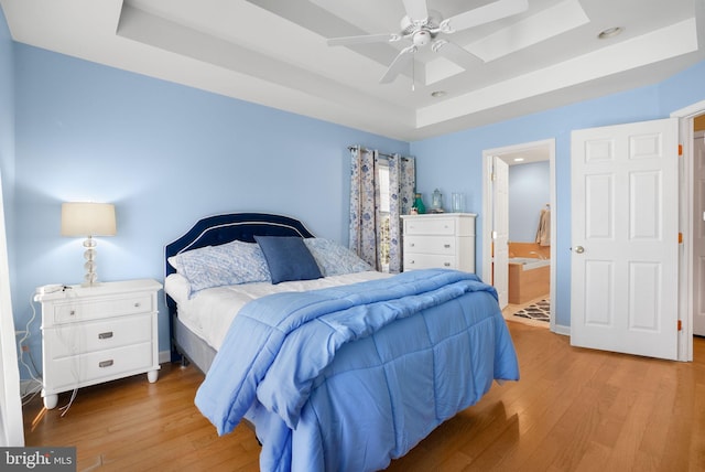 bedroom with light hardwood / wood-style floors, a raised ceiling, ceiling fan, and ensuite bathroom