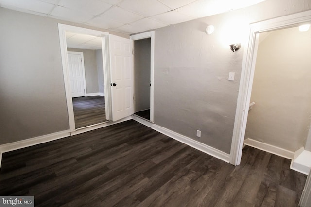 unfurnished bedroom with a drop ceiling, dark wood-type flooring, and a closet