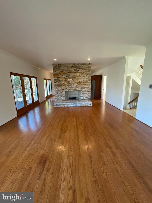 unfurnished living room with wood-type flooring, a stone fireplace, and crown molding