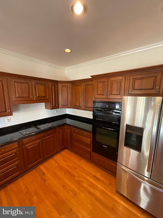 kitchen featuring stainless steel refrigerator with ice dispenser, light hardwood / wood-style flooring, dark stone countertops, ornamental molding, and double oven