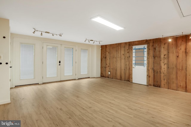 unfurnished room featuring wooden walls, french doors, and light wood-type flooring