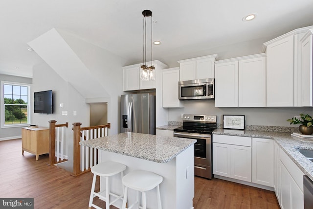 kitchen with white cabinets, appliances with stainless steel finishes, a kitchen island, and wood-type flooring