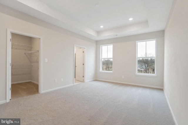 unfurnished bedroom with a raised ceiling, a spacious closet, light carpet, and a closet