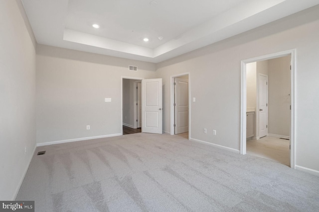 unfurnished bedroom featuring a raised ceiling, light colored carpet, and connected bathroom