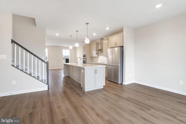 kitchen with stainless steel fridge, wall chimney exhaust hood, sink, pendant lighting, and an island with sink