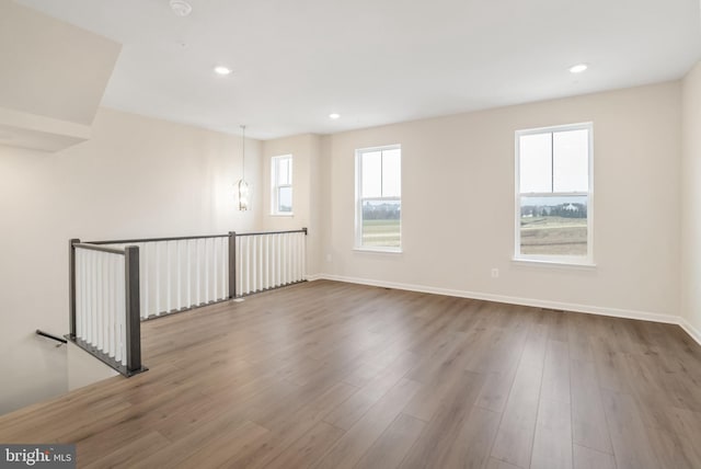 spare room featuring a healthy amount of sunlight, a notable chandelier, and hardwood / wood-style flooring