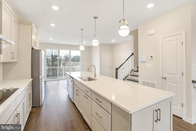 kitchen featuring appliances with stainless steel finishes, dark wood-type flooring, sink, a center island with sink, and hanging light fixtures