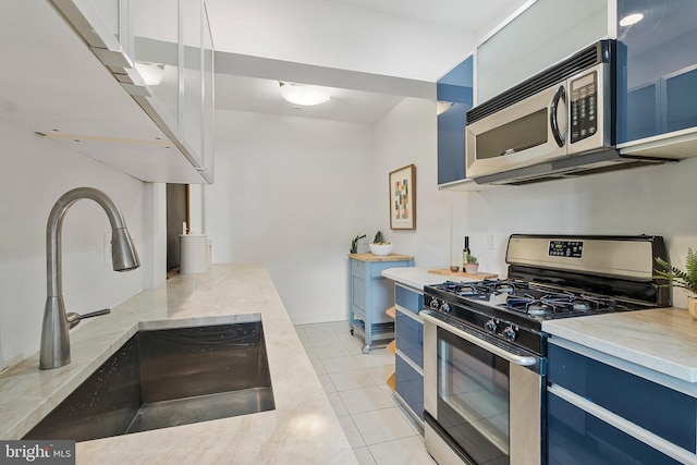 kitchen featuring blue cabinets, sink, light tile patterned flooring, and appliances with stainless steel finishes