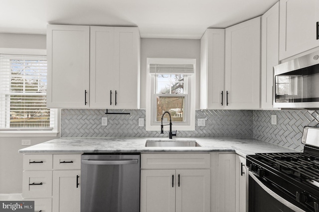 kitchen featuring white cabinetry, sink, light stone counters, backsplash, and appliances with stainless steel finishes