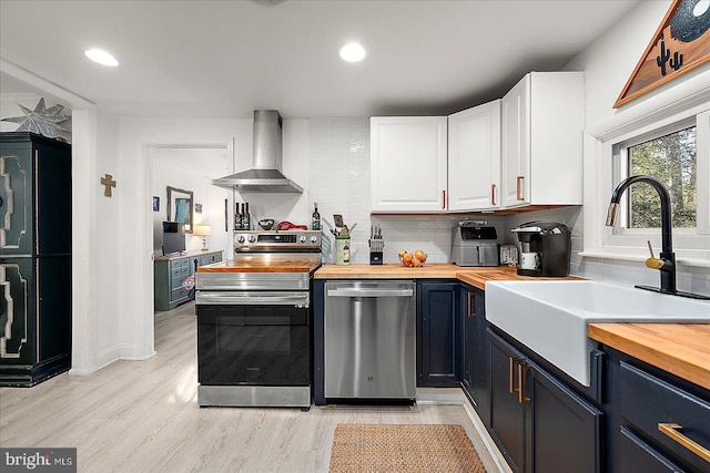 kitchen with wood counters, white cabinetry, appliances with stainless steel finishes, and wall chimney range hood