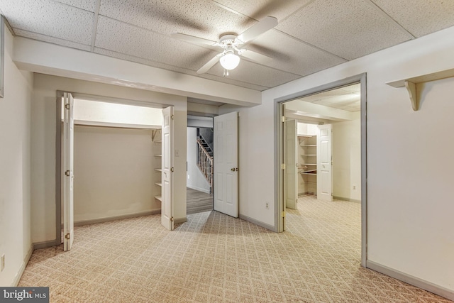 unfurnished bedroom featuring light carpet, a paneled ceiling, a closet, and ceiling fan