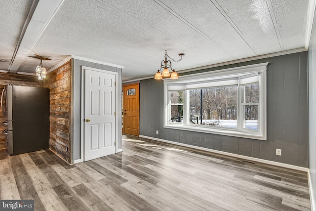 unfurnished dining area featuring wood walls, wood-type flooring, ornamental molding, and an inviting chandelier