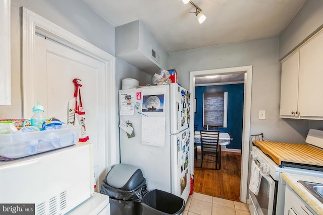 kitchen with white cabinets, white fridge, light tile patterned floors, and stainless steel range with electric cooktop