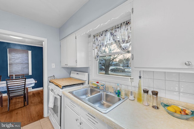 kitchen featuring white electric range oven, light tile patterned floors, white cabinets, and sink