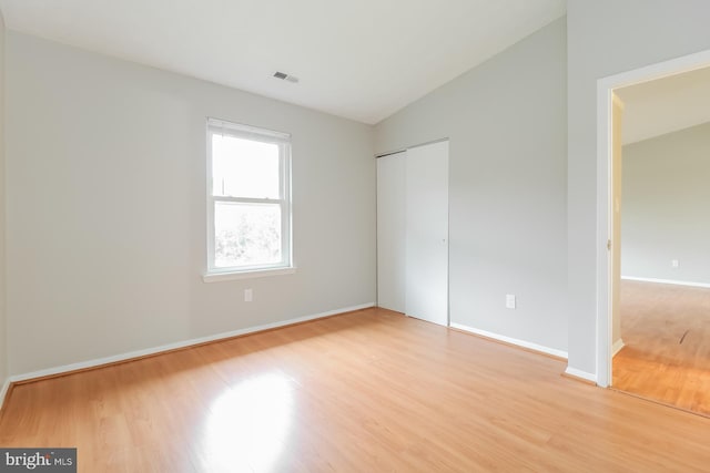 unfurnished bedroom with light hardwood / wood-style flooring, a closet, and lofted ceiling