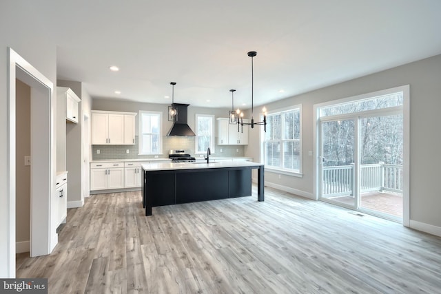 kitchen with wall chimney exhaust hood, hanging light fixtures, backsplash, white cabinets, and light wood-type flooring