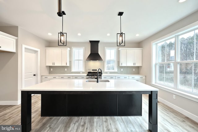 kitchen with sink, white cabinetry, a wealth of natural light, and wall chimney range hood