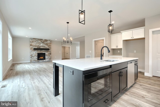 kitchen featuring white cabinetry, a kitchen island with sink, hanging light fixtures, and black microwave