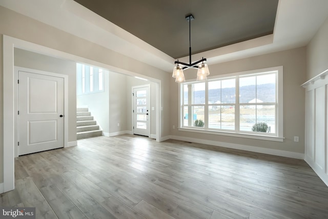 unfurnished dining area featuring light hardwood / wood-style floors, a raised ceiling, and a chandelier