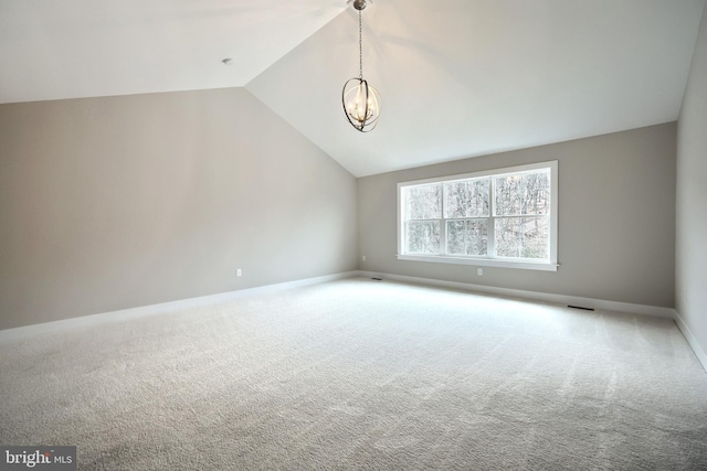 carpeted spare room featuring lofted ceiling and a chandelier