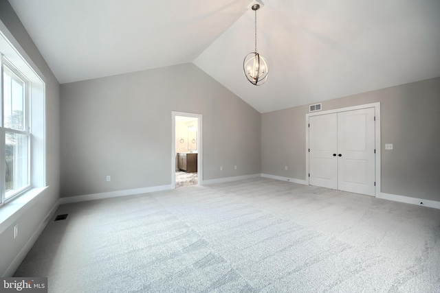 carpeted empty room featuring vaulted ceiling, plenty of natural light, and a notable chandelier