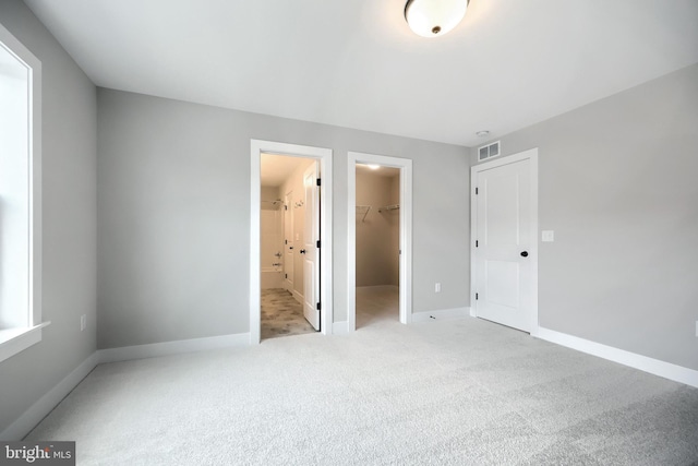 unfurnished bedroom featuring a walk in closet, ensuite bathroom, a closet, and light colored carpet