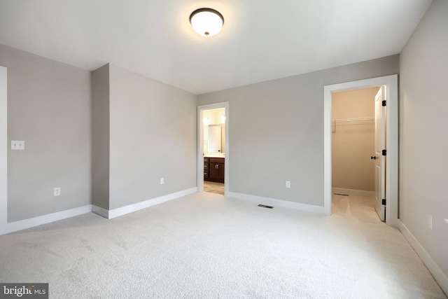 unfurnished bedroom featuring light carpet, connected bathroom, a spacious closet, and a closet