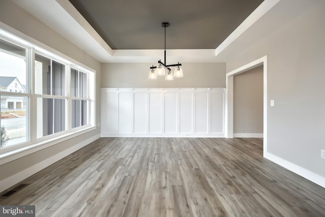 unfurnished dining area featuring a tray ceiling, a healthy amount of sunlight, light wood-type flooring, and a notable chandelier