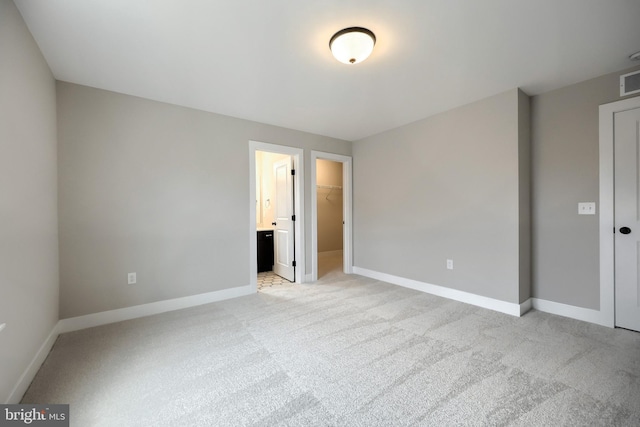 unfurnished bedroom featuring light colored carpet, a spacious closet, connected bathroom, and a closet