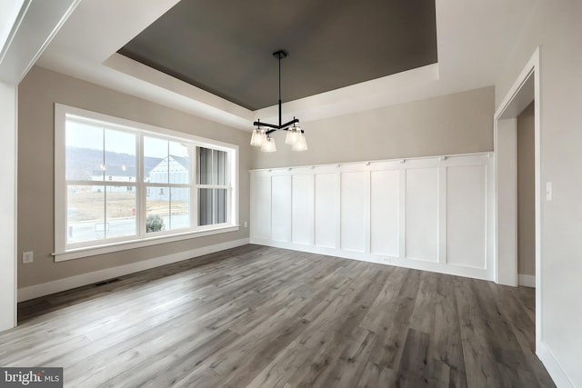 unfurnished dining area featuring a tray ceiling, light hardwood / wood-style floors, and a notable chandelier