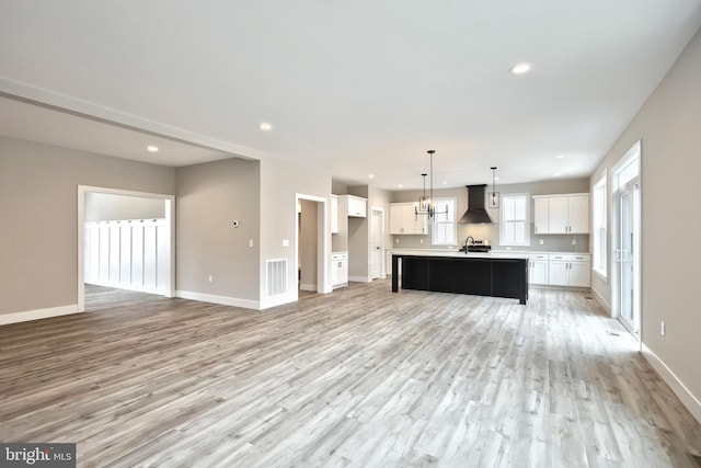 kitchen with light hardwood / wood-style flooring, premium range hood, an island with sink, decorative light fixtures, and white cabinets