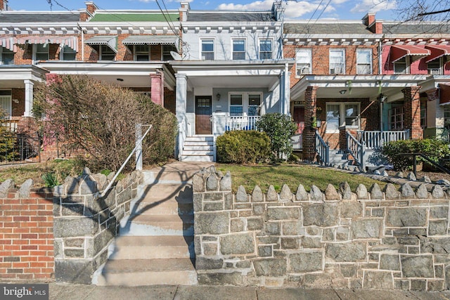 view of property featuring brick siding, a porch, and mansard roof