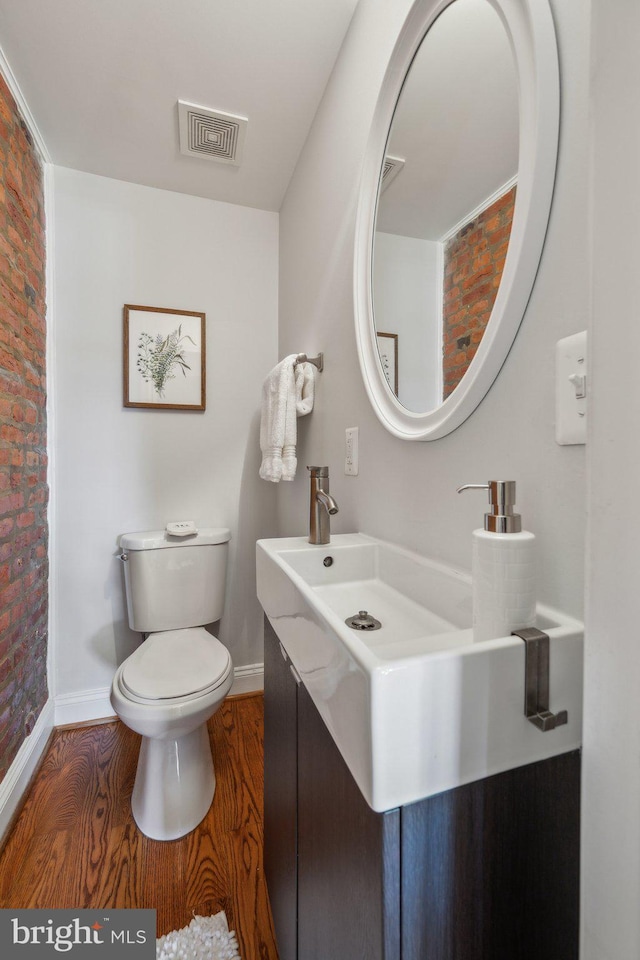 half bath featuring vanity, toilet, wood finished floors, and visible vents