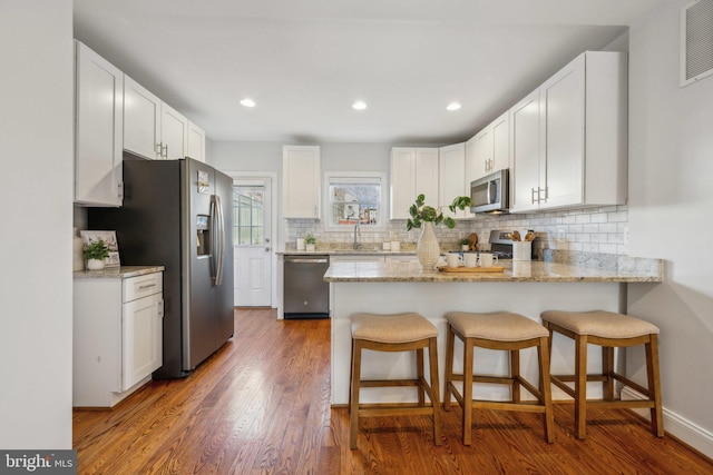 kitchen with light stone counters, wood finished floors, stainless steel appliances, a peninsula, and decorative backsplash