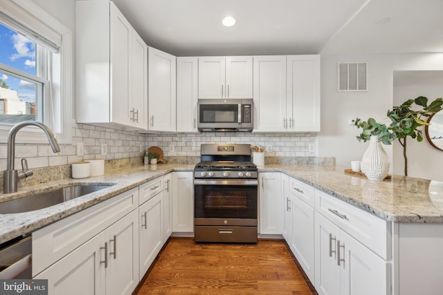 kitchen with visible vents, a sink, appliances with stainless steel finishes, a peninsula, and white cabinets