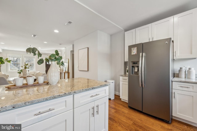 kitchen with light stone counters, visible vents, stainless steel fridge with ice dispenser, white cabinets, and light wood-style floors