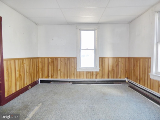 carpeted spare room featuring a baseboard radiator, a drop ceiling, and wood walls