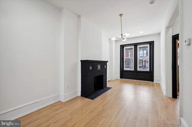 unfurnished living room featuring a chandelier, a brick fireplace, and light hardwood / wood-style flooring