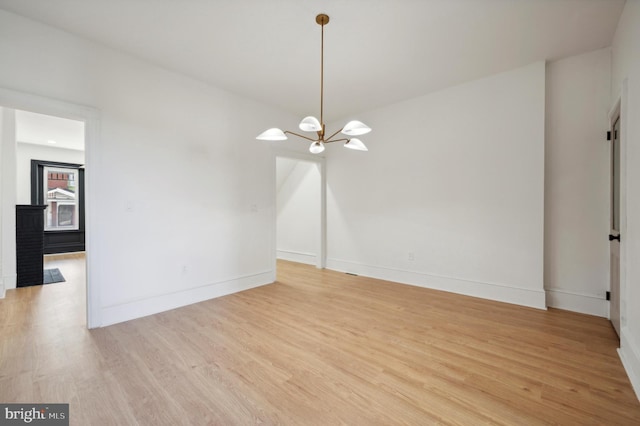 empty room with light hardwood / wood-style flooring and a chandelier